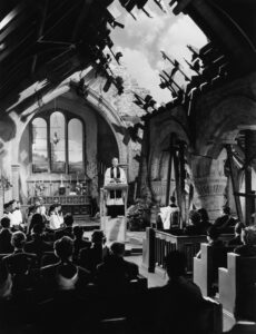 Photo of Henry Wilcoxon as the vicar, delivering an emotional sermon in the bombed-out church.