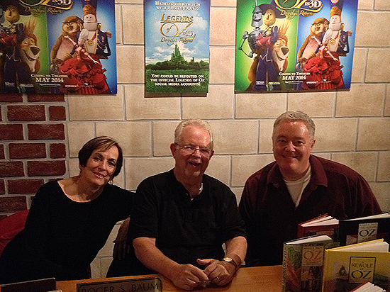 Charlene Baum, Roger S. Baum, and Paul Miles Schneider, special guests at this year's OZtoberFest. A 3D animated film adaptation of Roger's book "Dorothy of Oz" will hit movie theatres in May, now called "Legends of Oz: Dorothy's Return." Several promotional posters can be seen on the wall. Wamego, Kansas. 2013.